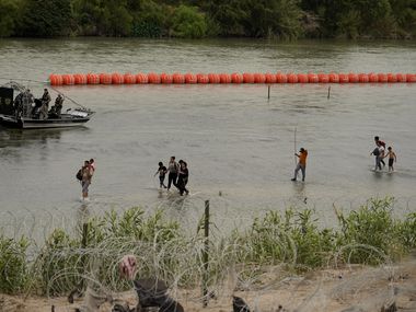 Migrantes que cruzaron el Río Grande desde México pasan por la barrera de boyas colocada por...