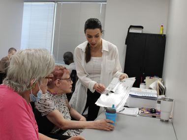 A woman in a white shirt helps two disabled adults with a project.