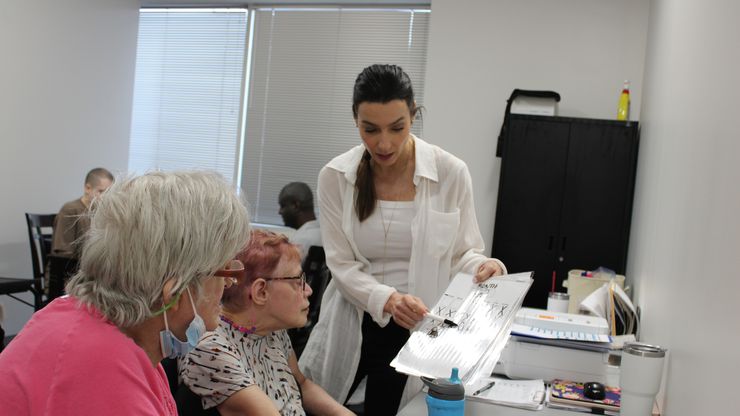 A woman in a white shirt helps two disabled adults with a project.