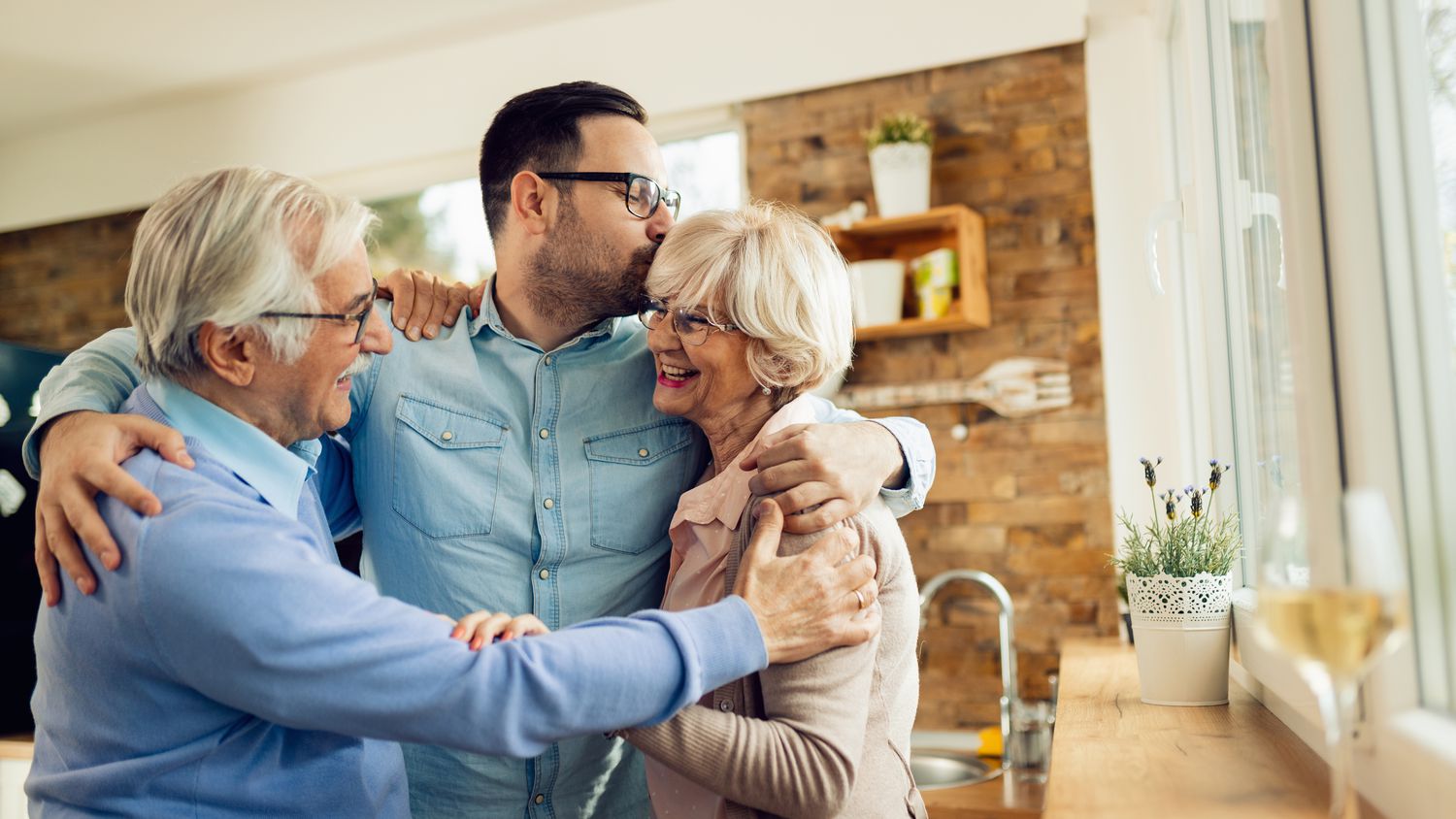 Happy mature couple embracing their adult son while greeting with him in the kitchen.