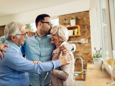 Happy mature couple embracing their adult son while greeting with him in the kitchen.