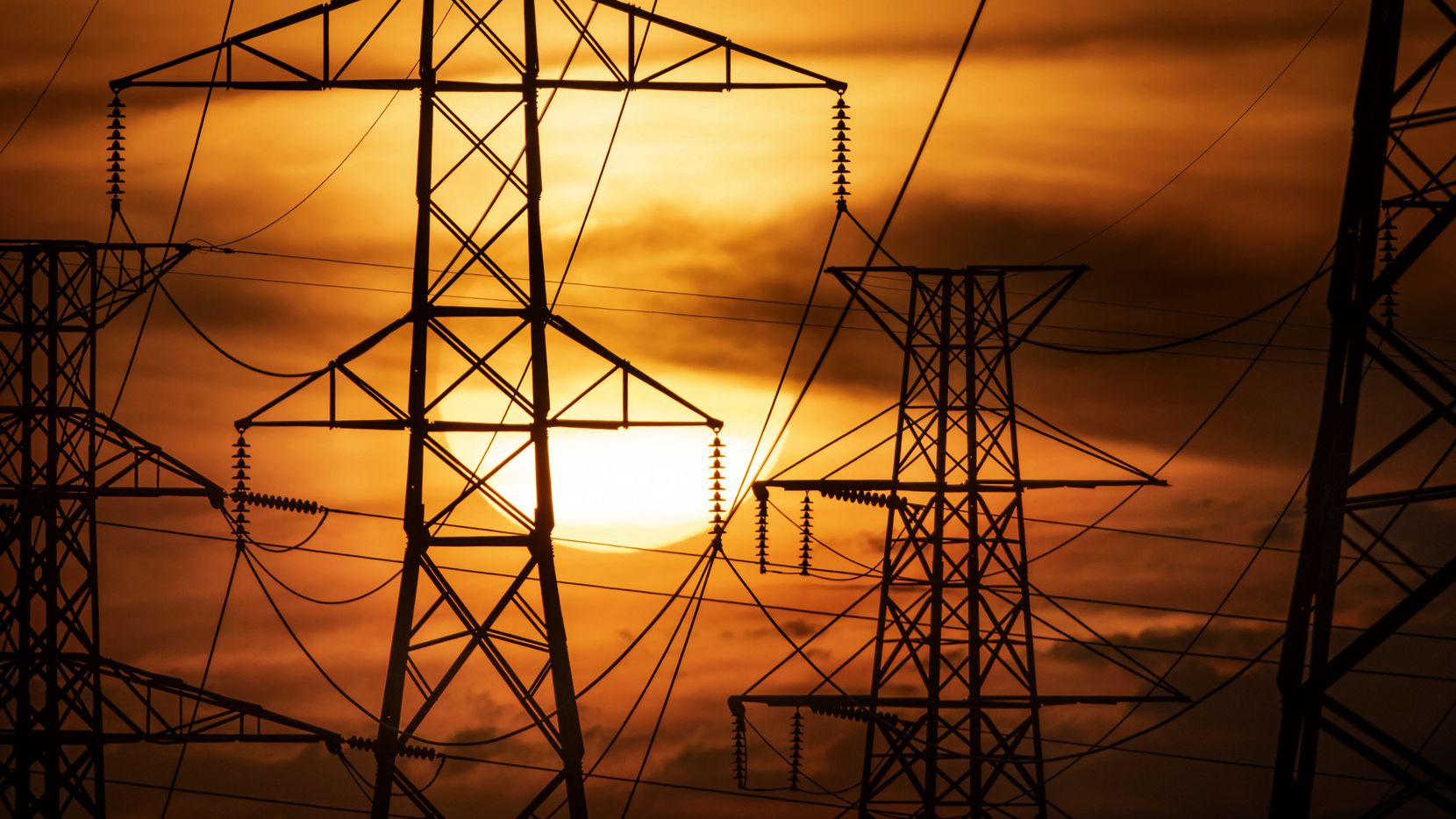 The sun sets behind electricity towers along Mountain Creek Parkway in Dallas on Wednesday,...